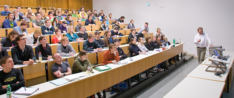 Ein Vortragender in einem Hörsaal erklärt Studierenden Inhalte